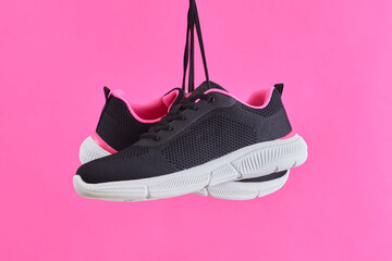 Pair female sports sneakers for run and fitness hanging by shoelaces on pink background. Fashion stylish sport shoes.