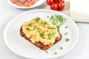 Scrambled eggs with microgreen and bacon on bread