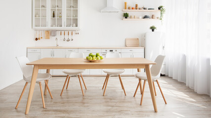 Scandinavian home interior. White and wooden kitchen furniture, plate with apples on dinning table,...