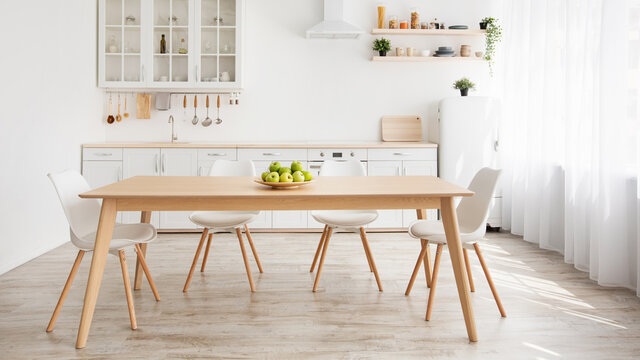 Scandinavian home interior. White and wooden kitchen furniture, plate with apples on dinning table, panorama