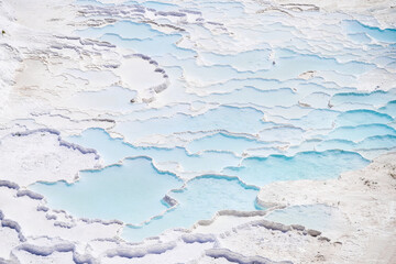 A view of the travertines. Pamukale, Turkey. Blue water in the terraces. A popular place for tourism. White rocks and water.