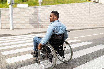 Fototapeta na wymiar Young disabled black man in wheelchair using crosswalk outdoors. Quality of life and impairment concept