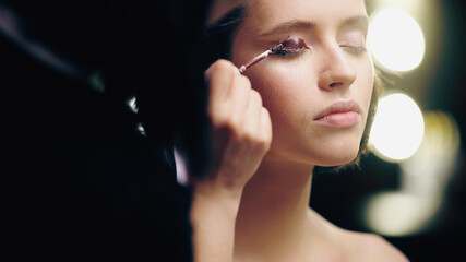 blurred makeup artist applying dark liquid eye shadow on eyelid of model