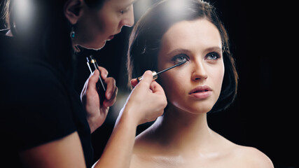 makeup artist applying mascara on eyelashes of model