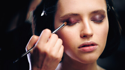 makeup artist applying eye shadow with cosmetic brush on model