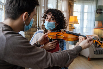 Happy woman play violin under music teacher's instructions in mask during coronavirus at home