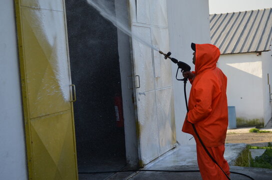 Rear View Of Man Working On Wall Washing The Chicken Coop With Foam Washer