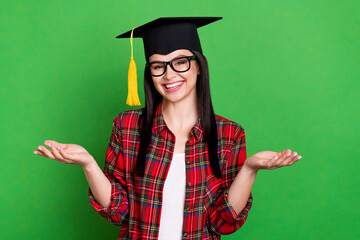 Photo of brunette clueless young lady shrug shoulders wearing graduation cap spectacles red shirt isolated on green color background