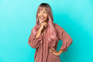 Young mixed race woman with pink hair isolated on blue background thinking an idea while looking up