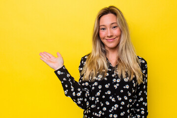 Young australian woman isolated showing a copy space on a palm and holding another hand on waist.