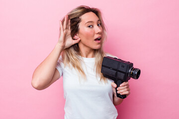 Young australian woman filming with a vintage video camera isolated trying to listening a gossip.