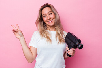 Young australian woman filming with a vintage video camera isolated joyful and carefree showing a...