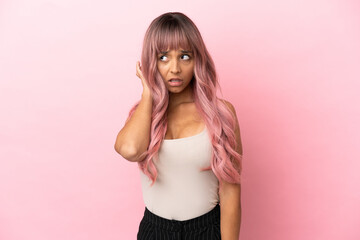 Young mixed race woman with pink hair isolated on pink background having doubts