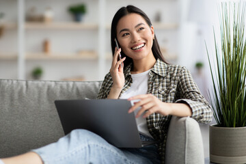 Beautiful young asian woman having phone conversation, using laptop