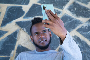 African-American man sitting on a a park bench taking a selfie with his mobile phone. He is looking at the camera very happy and content.