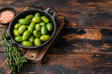 Green big olives in bowl with thyme. Dark wooden background. Top view. Copy space