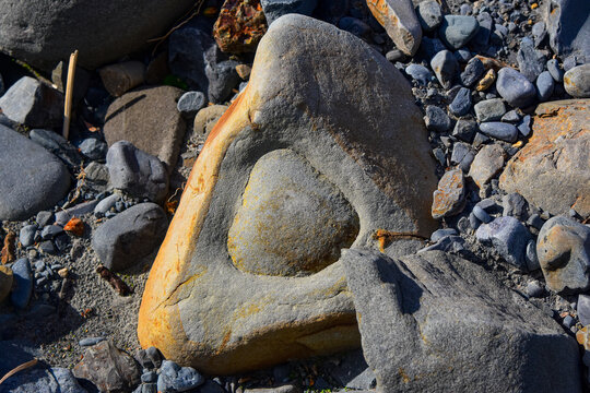 Triangle shaped rock with another triangle worn into the center of it surrounded by regular rocks and gravel in a river bed