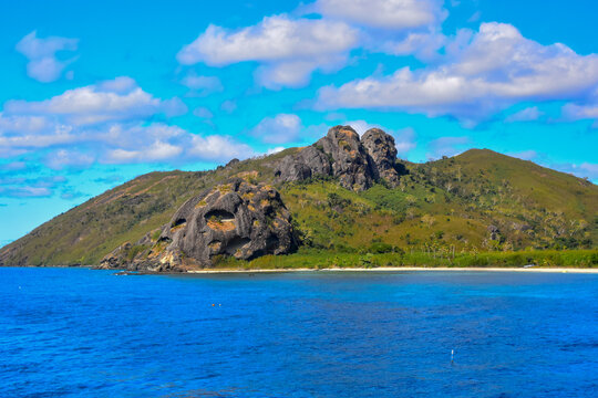Rocky almost face-like boulders emerging from tropical South Pacific Island with fluffy white clouds in the sky