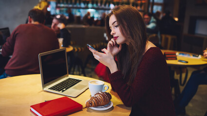 Pensive woman with hand at chin browsing smartphone