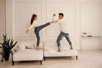 young couple in safety masks fighting on couch while fooling around at home