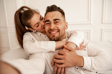 pretty woman biting ear of cheerful man while having fun at home