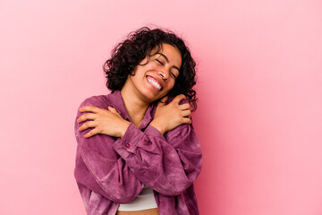 Young curly latin woman isolated on pink background hugs, smiling carefree and happy.