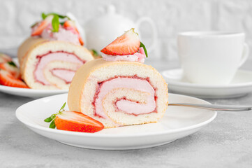Cake roll with fresh strawberries, jam and cream cheese on a white plate on a gray background. Copy space.