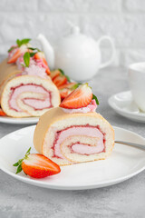 Cake roll with fresh strawberries, jam and cream cheese on a white plate on a gray background. Copy space.