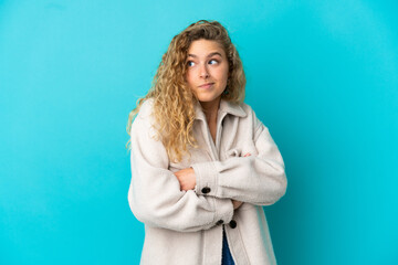 Young blonde woman isolated on blue background making doubts gesture while lifting the shoulders