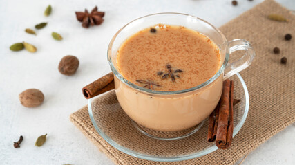 Masala tea chai in a glass cup with ingredients for cooking. Cinnamon sticks, ginger, cardamom,...