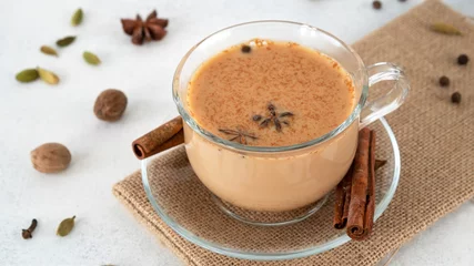 Fotobehang Masala tea chai in a glass cup with ingredients for cooking. Cinnamon sticks, ginger, cardamom, anise, honey, cloves. Traditional Indian drink - spicy black tea with spices and milk. Close up. © Irina