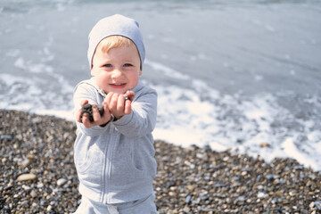 child blond boy playing with rocks and sand on the beach on a sunny day in spring or autumn