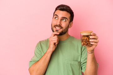 Young caucasian man holding an almond jar isolated on pink background relaxed thinking about something looking at a copy space.