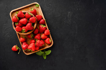 Fresh strawberry on a black concrete background. Strawberries with leaves on wooden plate.