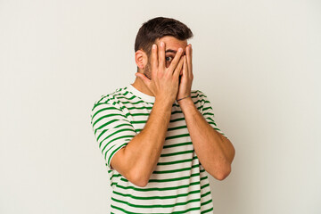 Young caucasian man isolated on white background blink through fingers frightened and nervous.