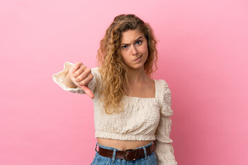 Young blonde woman isolated on pink background showing thumb down with negative expression