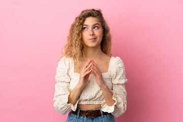 Young blonde woman isolated on pink background scheming something