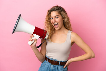 Young blonde woman isolated on pink background holding a megaphone and smiling