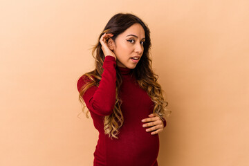 Young mexican pregnant woman isolated on beige background trying to listening a gossip.