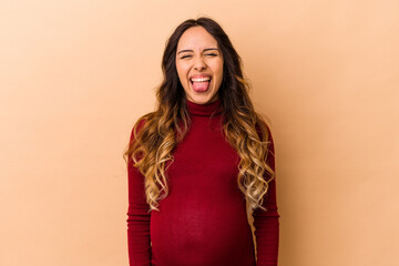 Young mexican pregnant woman isolated on beige background funny and friendly sticking out tongue.