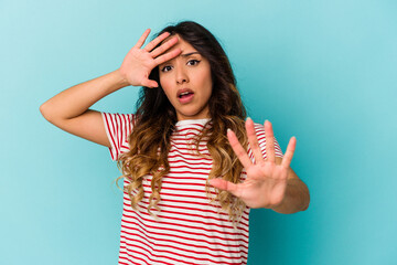 Young mexican woman isolated on blue background being shocked due to an imminent danger