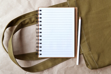 Reusable shopping bag made of cotton, a notebook with a blank layout, a pencil on craft paper.An...