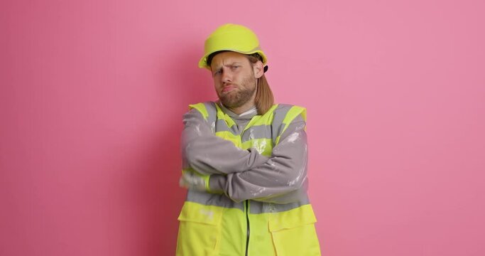 Shocked redhead handyman stares at camera wears uniform and headwear makes offensive expression being busy doing house construction poses against pink background. Professional builder indoor