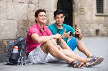 Men friends are talking and drinking a beer in time walking at a city