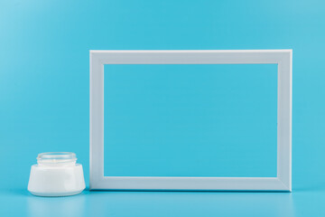White jar of skin cream and white photo frame on blue background.