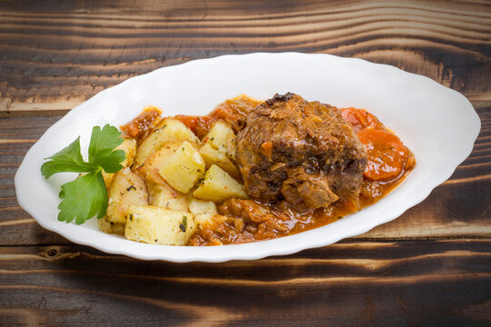 Braised beef tails with vegetables and potatoes in a white plate on a wooden background