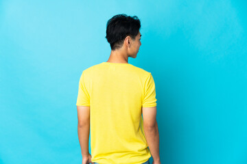 Young Chinese man isolated on blue background in back position and looking side