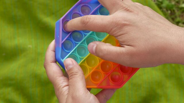 Girl, woman, teenager develops finger motility with colorful poppit game. Close up bunner shot of kid hands playing with colorful pop It fidget toy