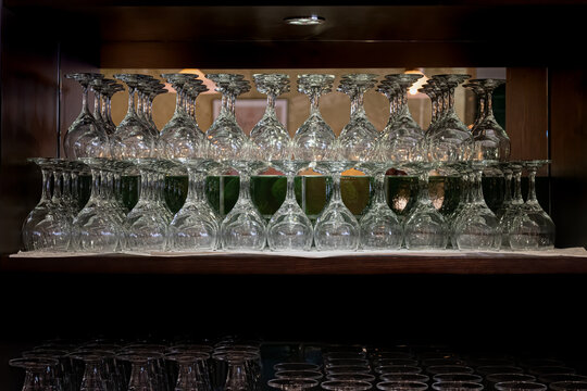 Many fragile shiny wine glass, lit on a dark shelf.