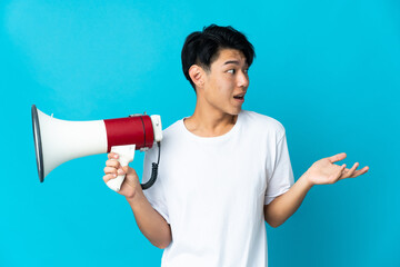 Young Chinese man isolated on blue background holding a megaphone and with surprise facial expression